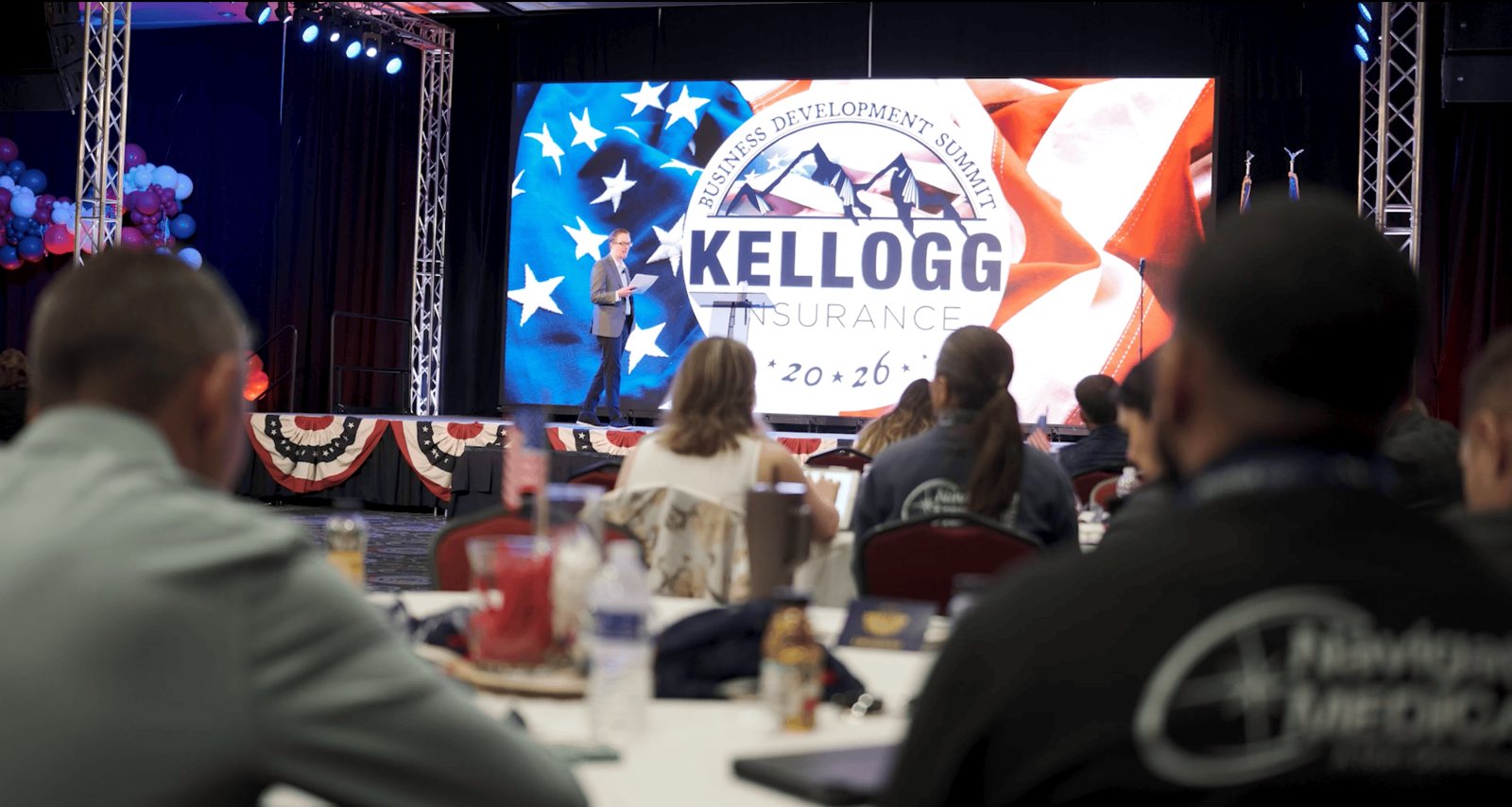 Keynote on stage in front of the branded Kellogg Insurance LED wall