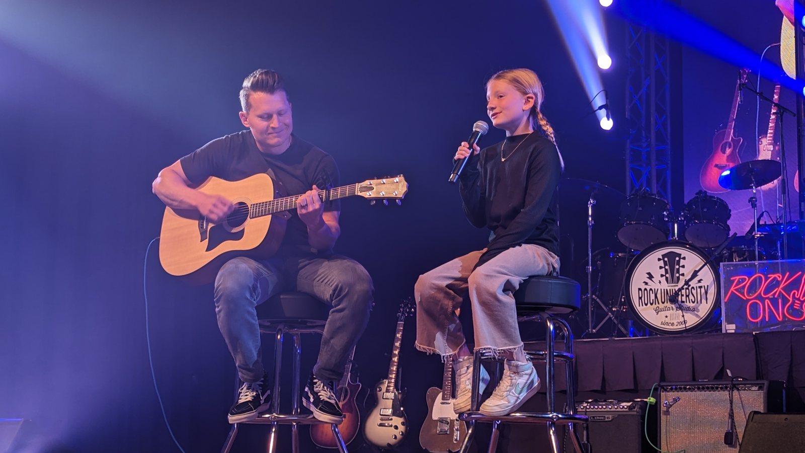 A teacher and student performing an acoustic duet on stage
