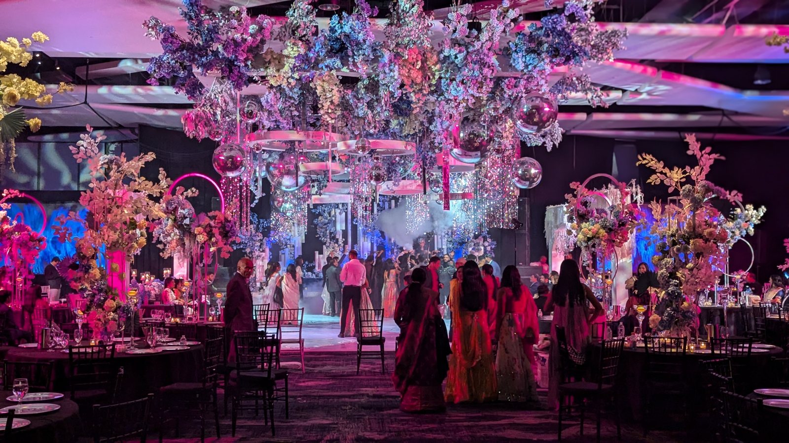 A wedding reception washed in pink and purple uplighting with floral centerpieces and haze